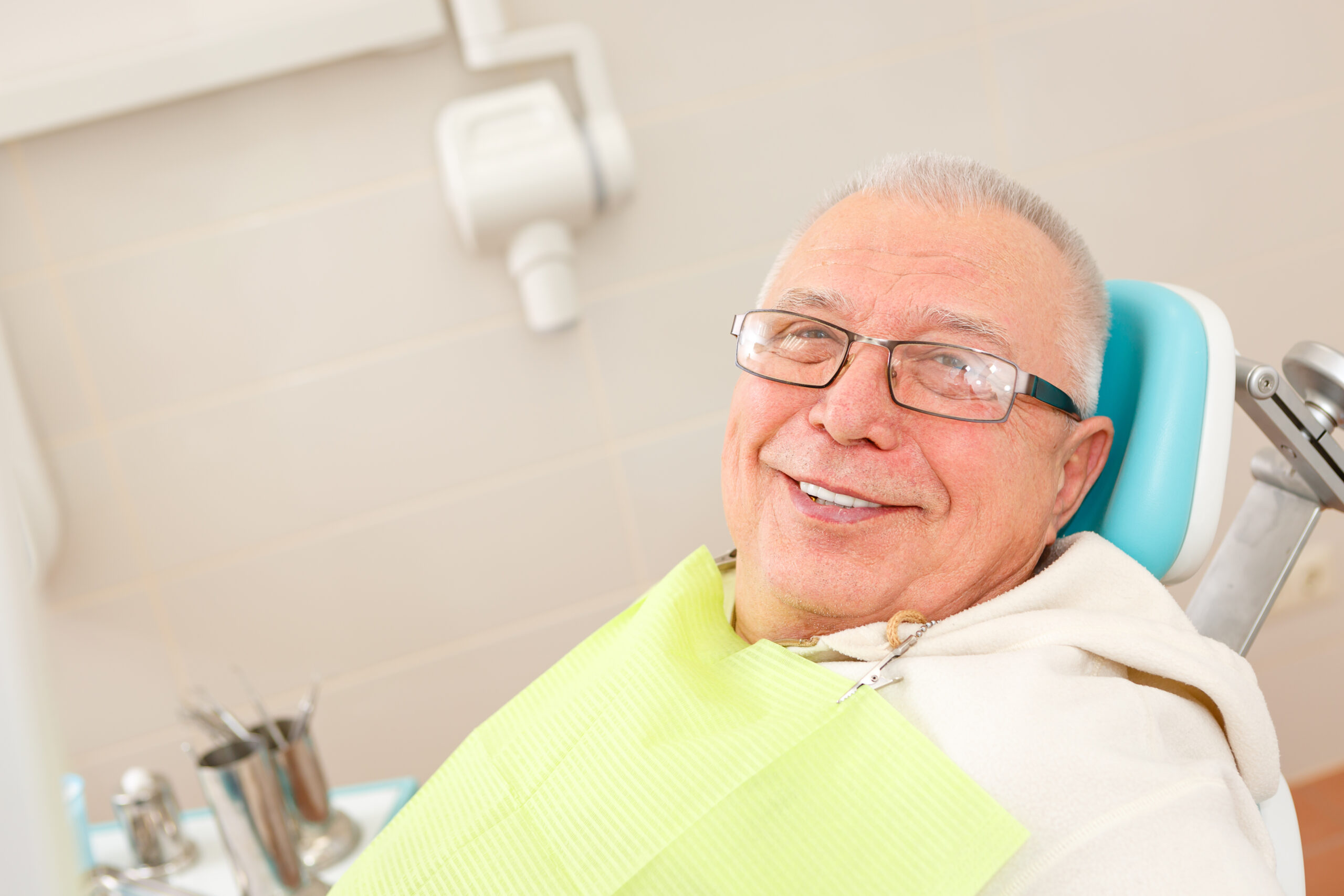 Old senior man with glasses sitting in a dental chair in a dentist's office.