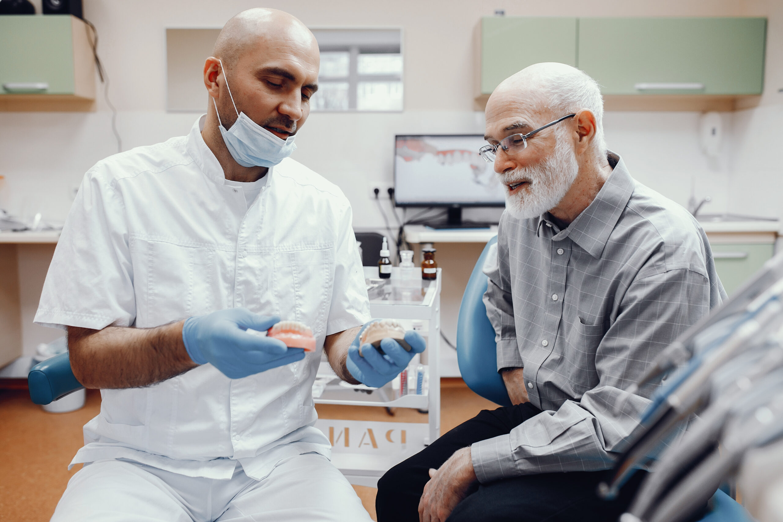 dentist showing dentures to an Old man sitting in a dentistry room