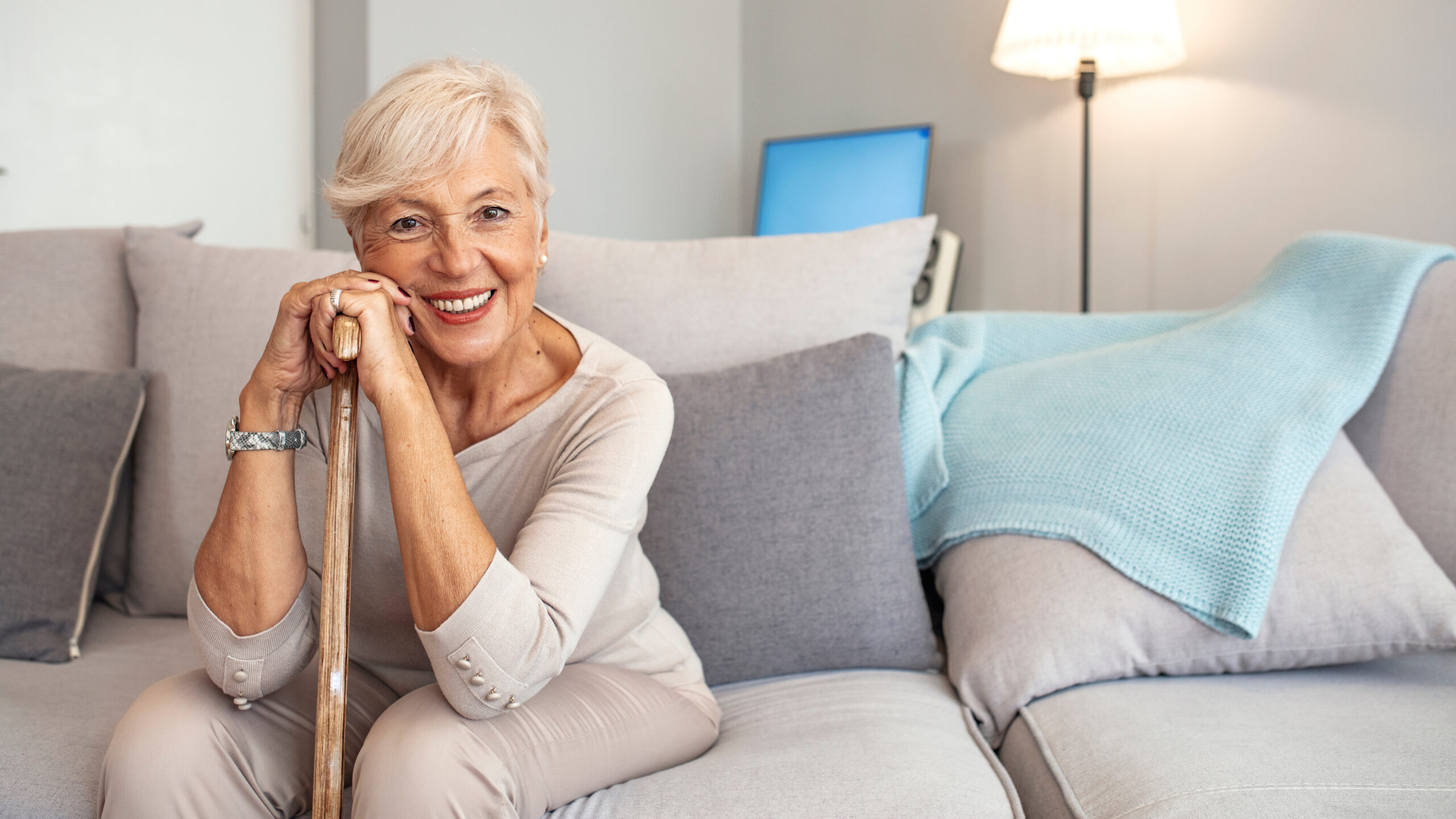 Portrait of a beautiful smiling senior woman with walking cane on light background at home. Old woman sitting with her hands on a cane