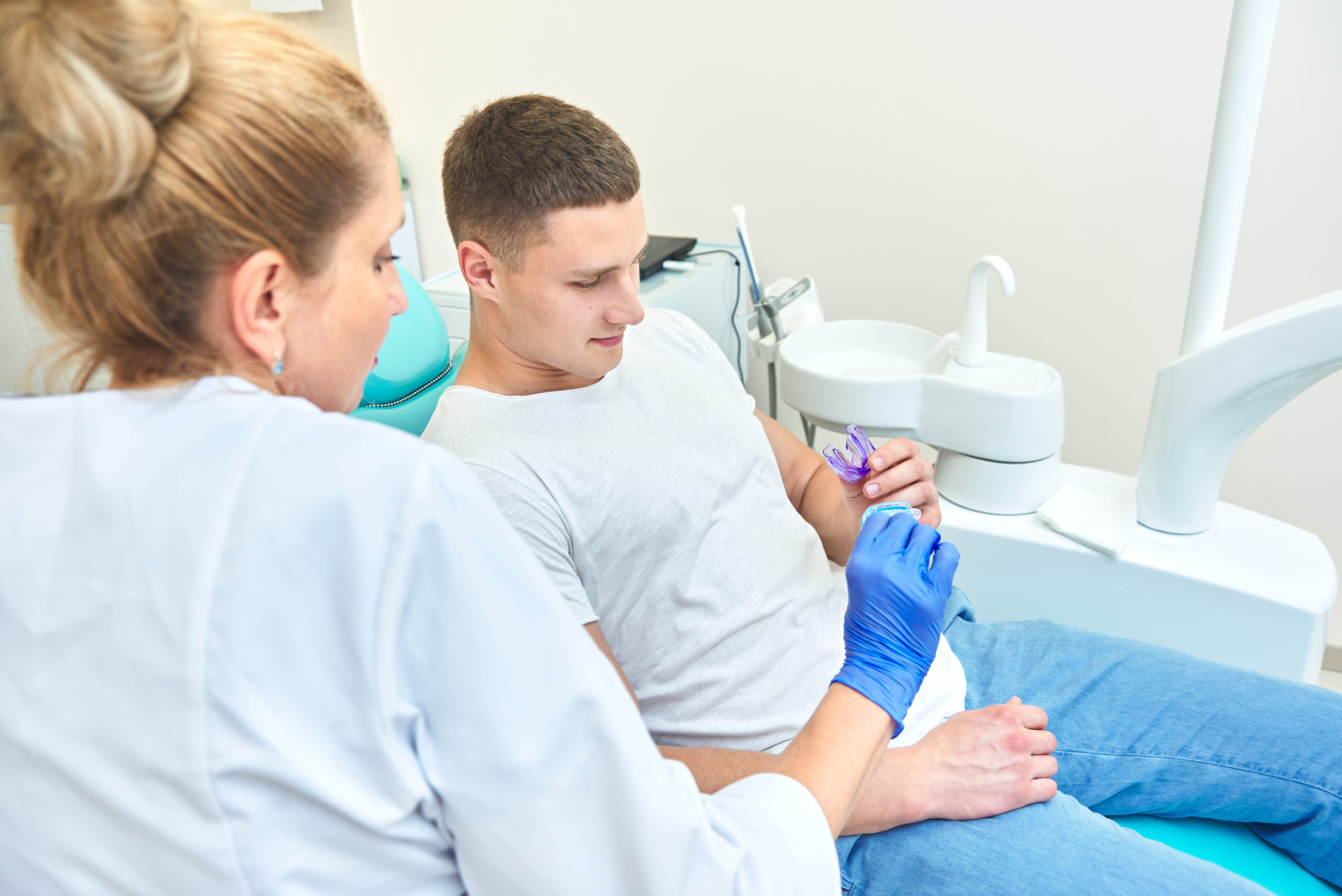 dentist showing a mouthguard to a patient sitting in the dental chair in the office