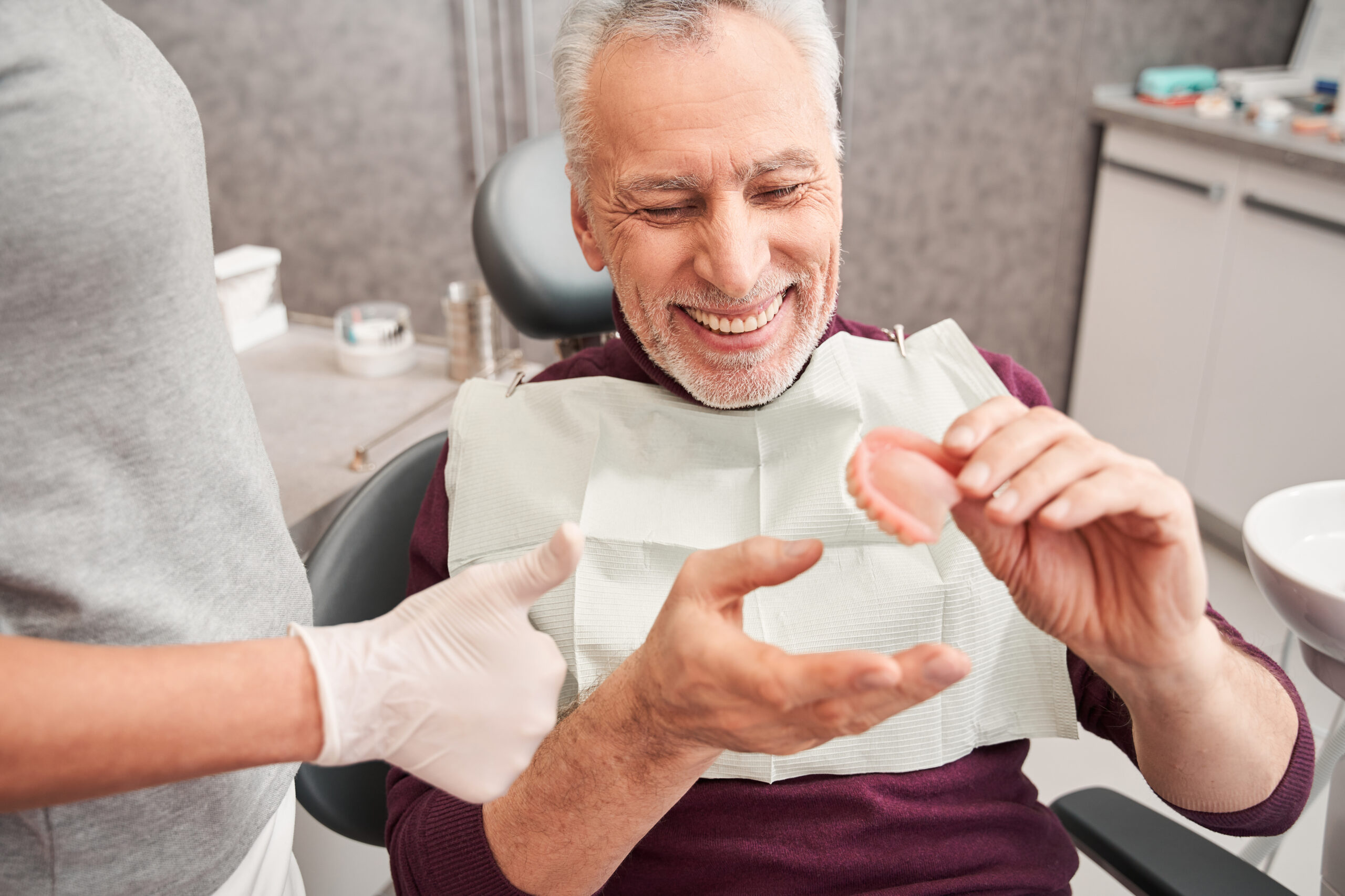 dentist showing to senior grey haired patient teeth dentures while working at the dental clinic