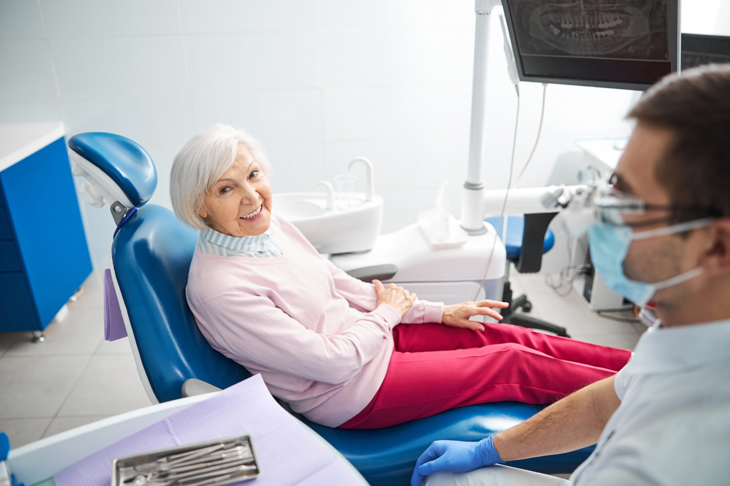 Woman sitting in a stomatological chair and putting right hand in left arm with dentist in mask nearby