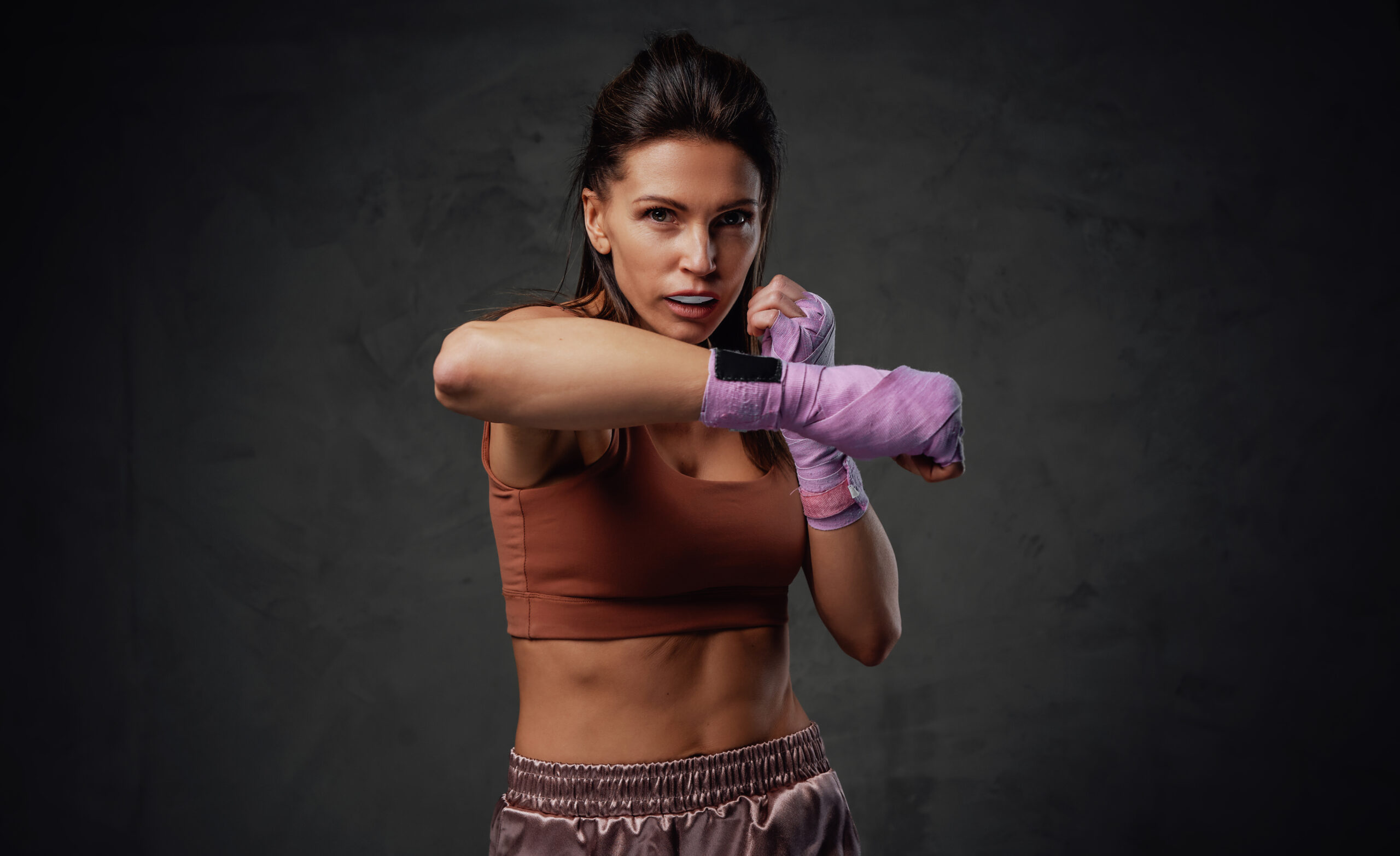 Female sportsperson with muscular build wearing activewear poses in dark background