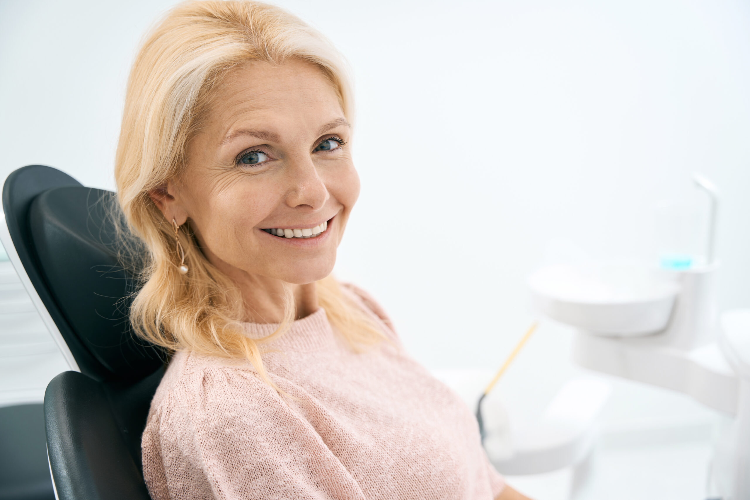 Portrait of happy woman sitting at dental chair and waiting for partial dentures procedure