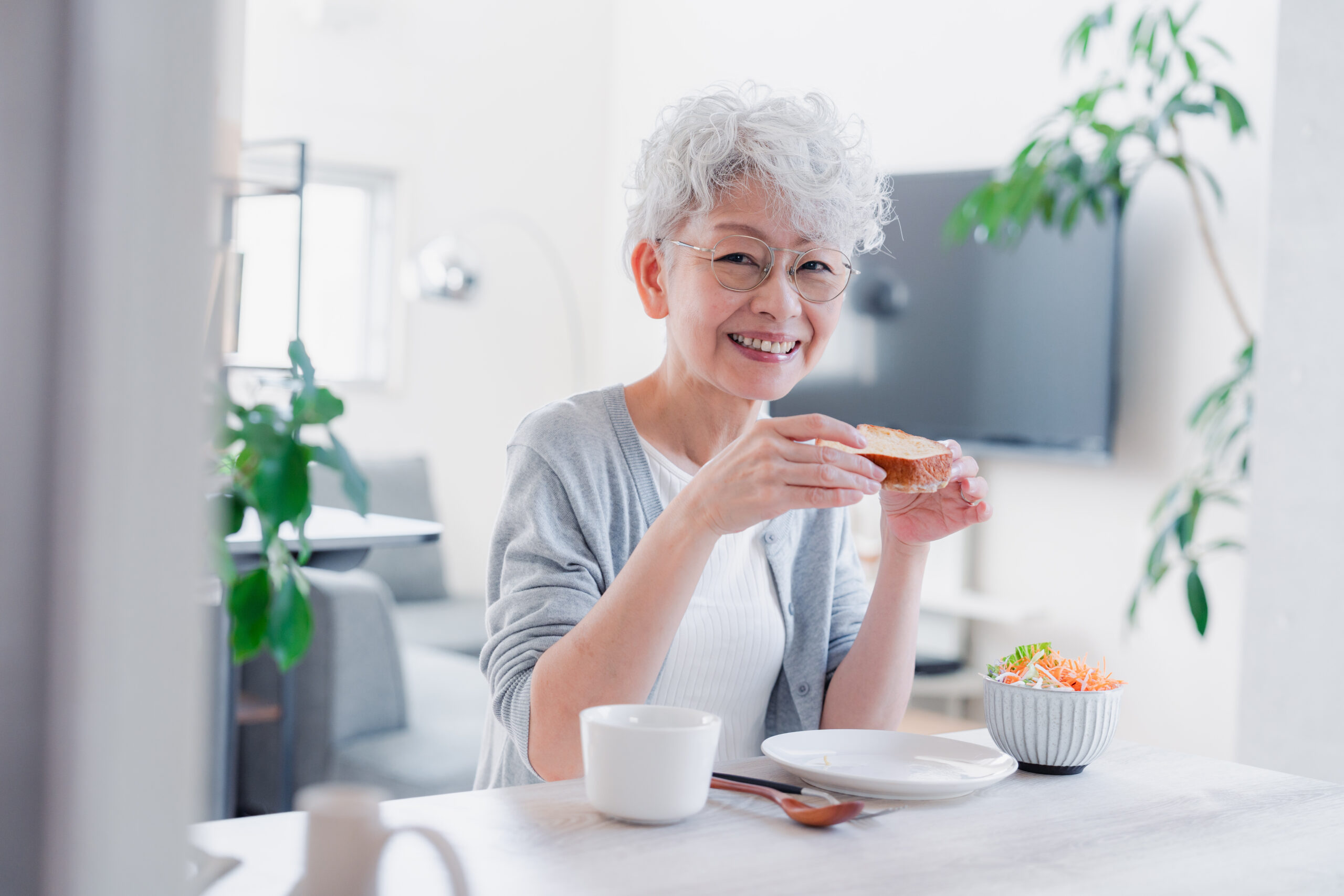 elderly woman holding a piece of bread while showing her smile with dentures