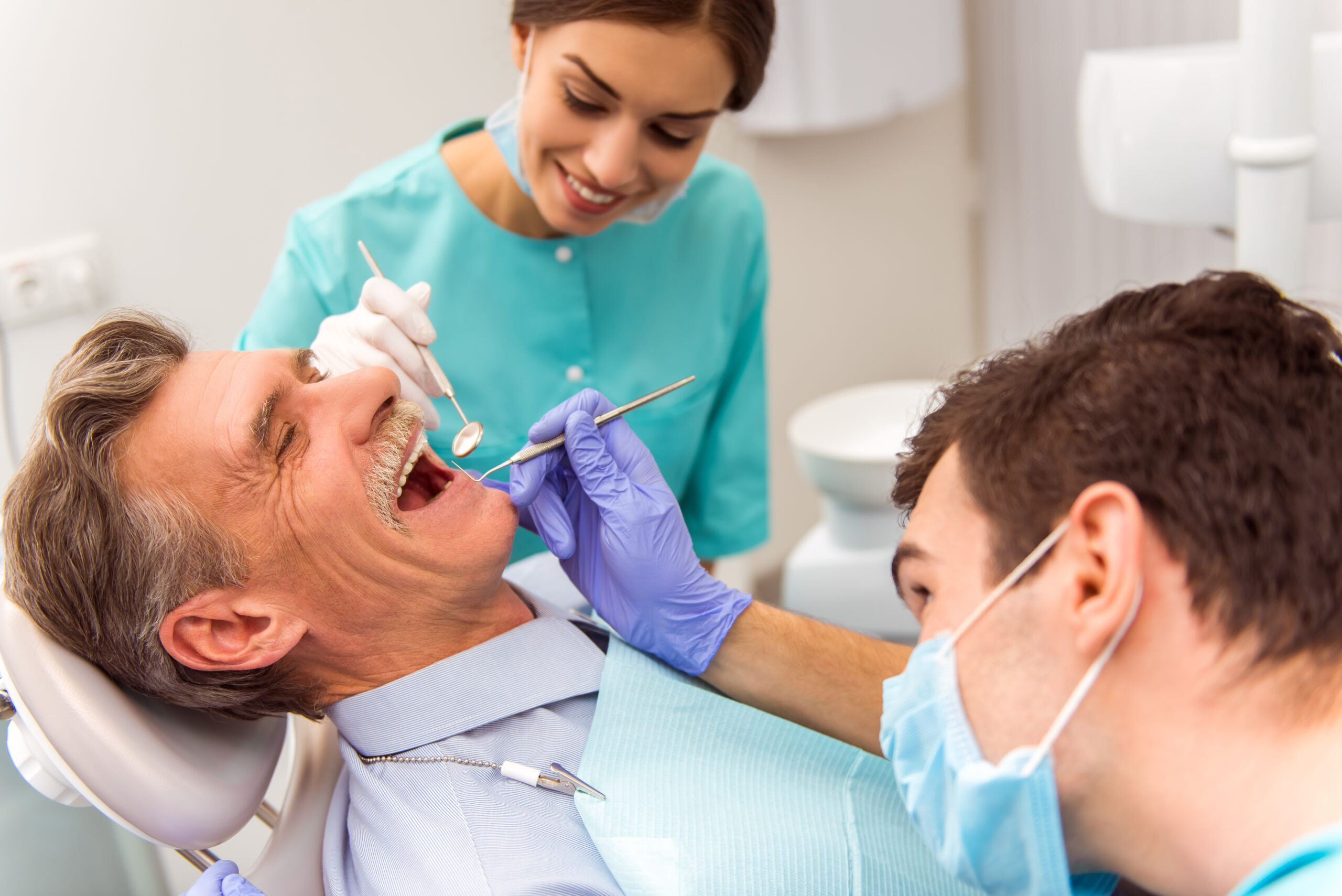 Young dentist and his assistant treating elderly man