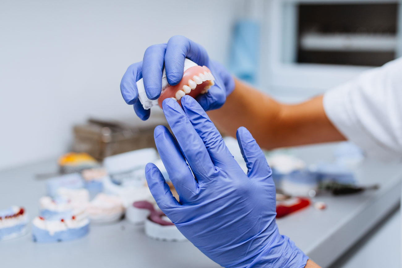 Gloved hands crafting a custom upper denture in the Galon Dental Prosthetics lab